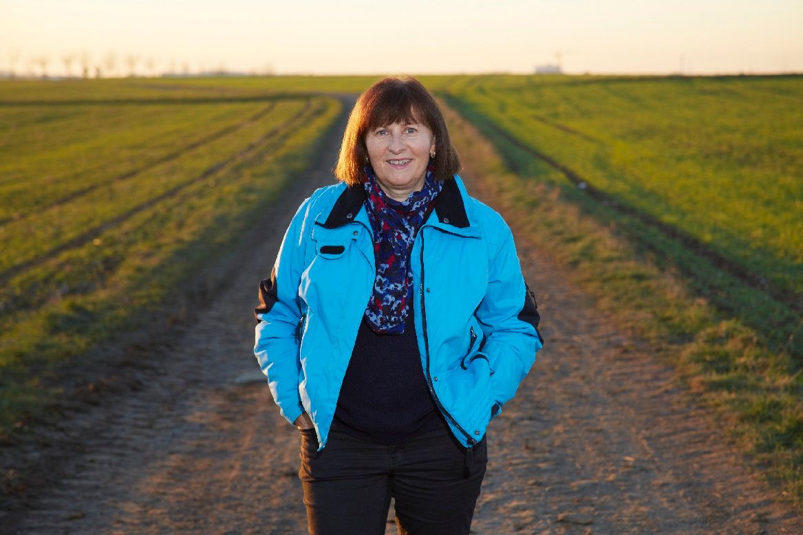 Helga Kröner-Schock steht auf einem Feldweg in einer ländlichen Umgebung. Im Bild eingeblendet ist das Zitat: „Ich möchte alle mutlosen Krebspatienten dazu motivieren, den Kopf nicht in den Sand zu stecken, sondern zu kämpfen!“