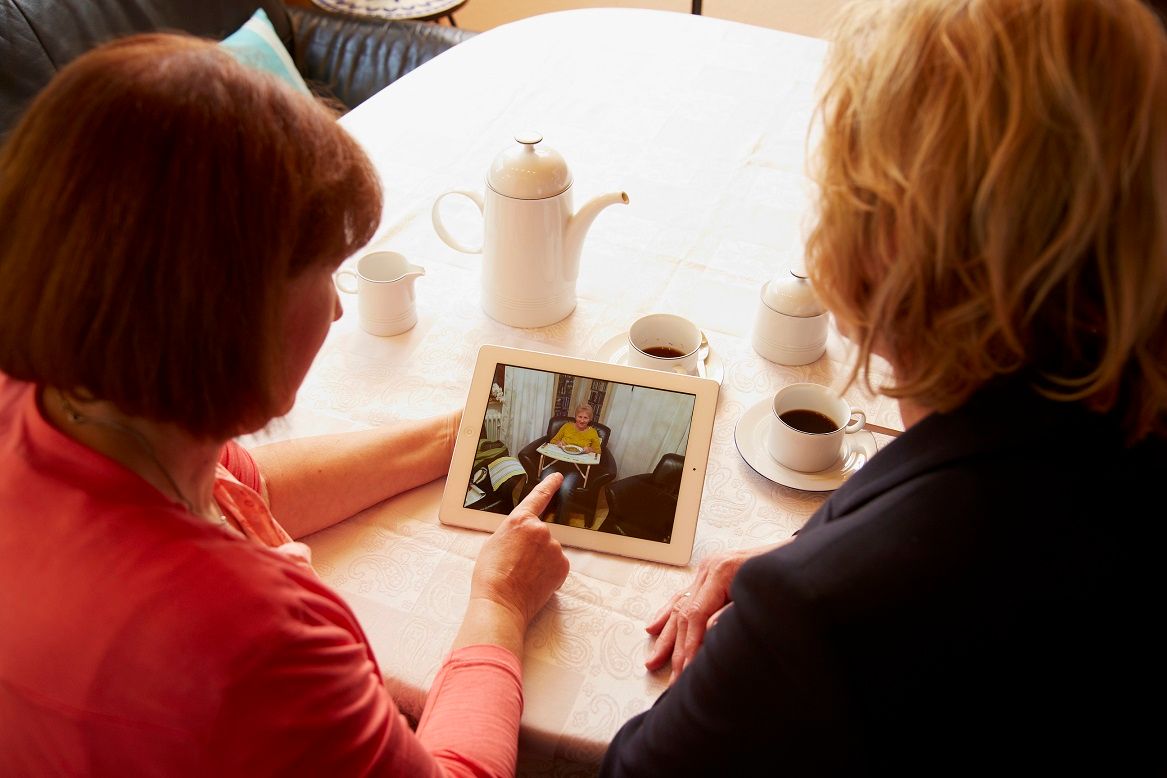 Helga Kröner-Schock betrachtet gemeinsam mit ihrer besten Freundin Fotos auf einem Tablet. Im Bild eingeblendet ist das Zitat: „Dass es mir wieder besser gehen würde, hätte ich nicht zu hoffen gewagt.“