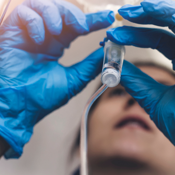 Eine Labormitarbeiterin mit blauen Einmalhandschuhen hält einen Infusionsschlauch. Im Bild ist in der Mitte die Tropfkammer zu sehen.