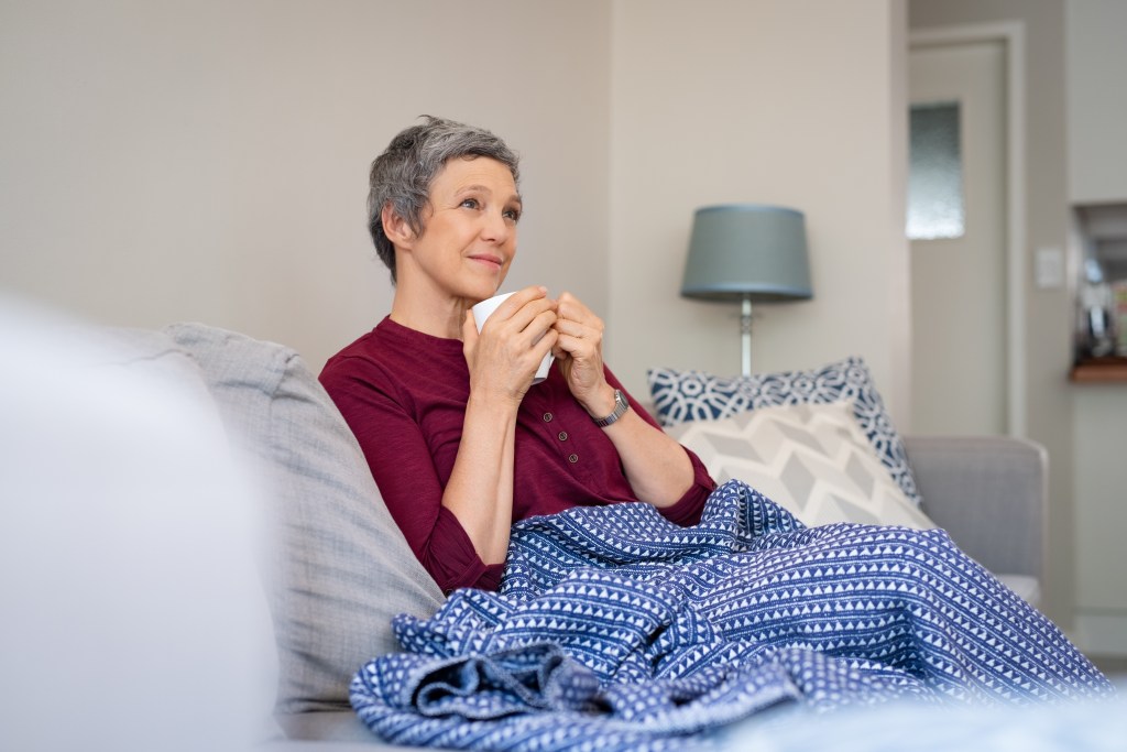 Frau mit Tasse und Decke auf dem Sofa