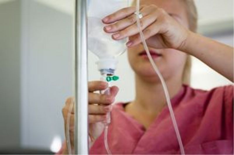 Eine Pflegekraft hält eine Infusion samt Leitung und ist bereit, einen Patienten in einer klinischen Umgebung zu versorgen.