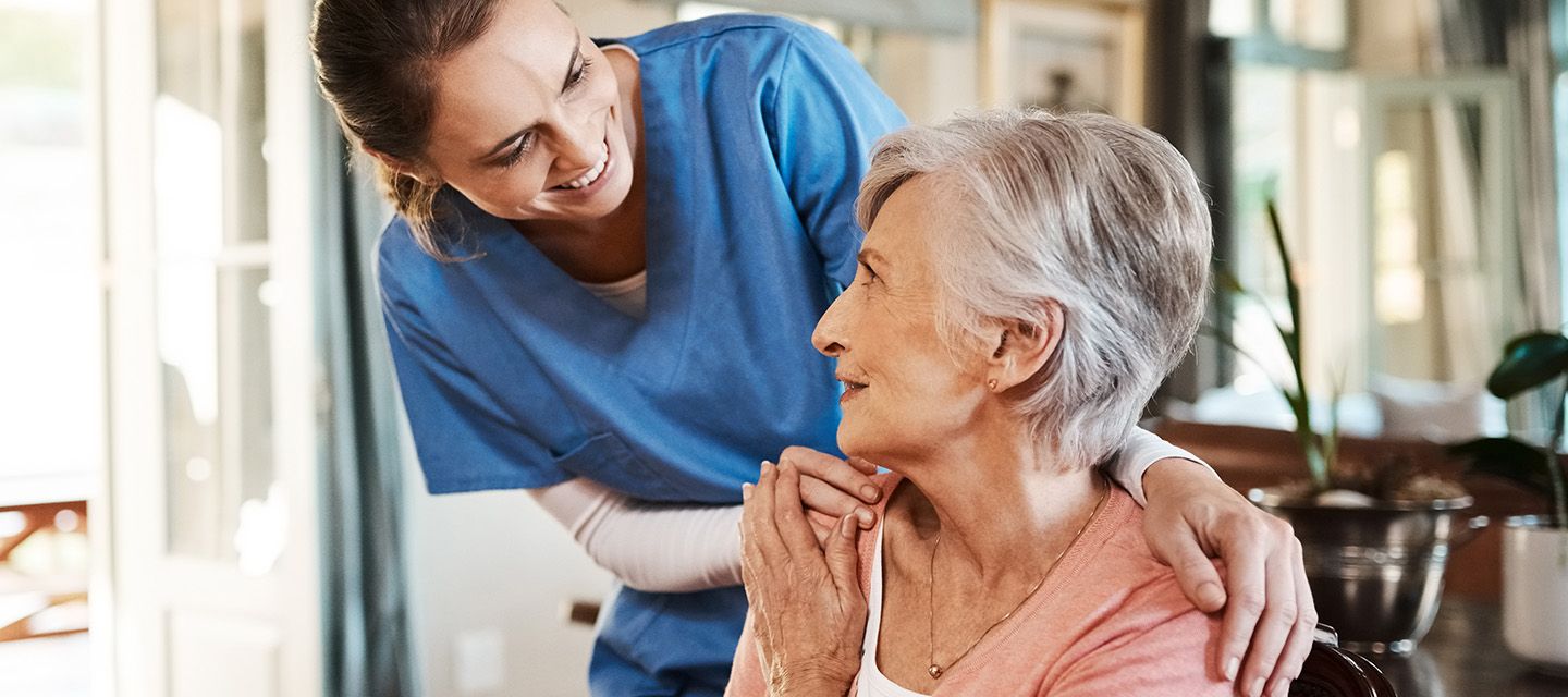 Lächelnde Patientin mittleren Alters und Krankenschwester im blauen Kittel.