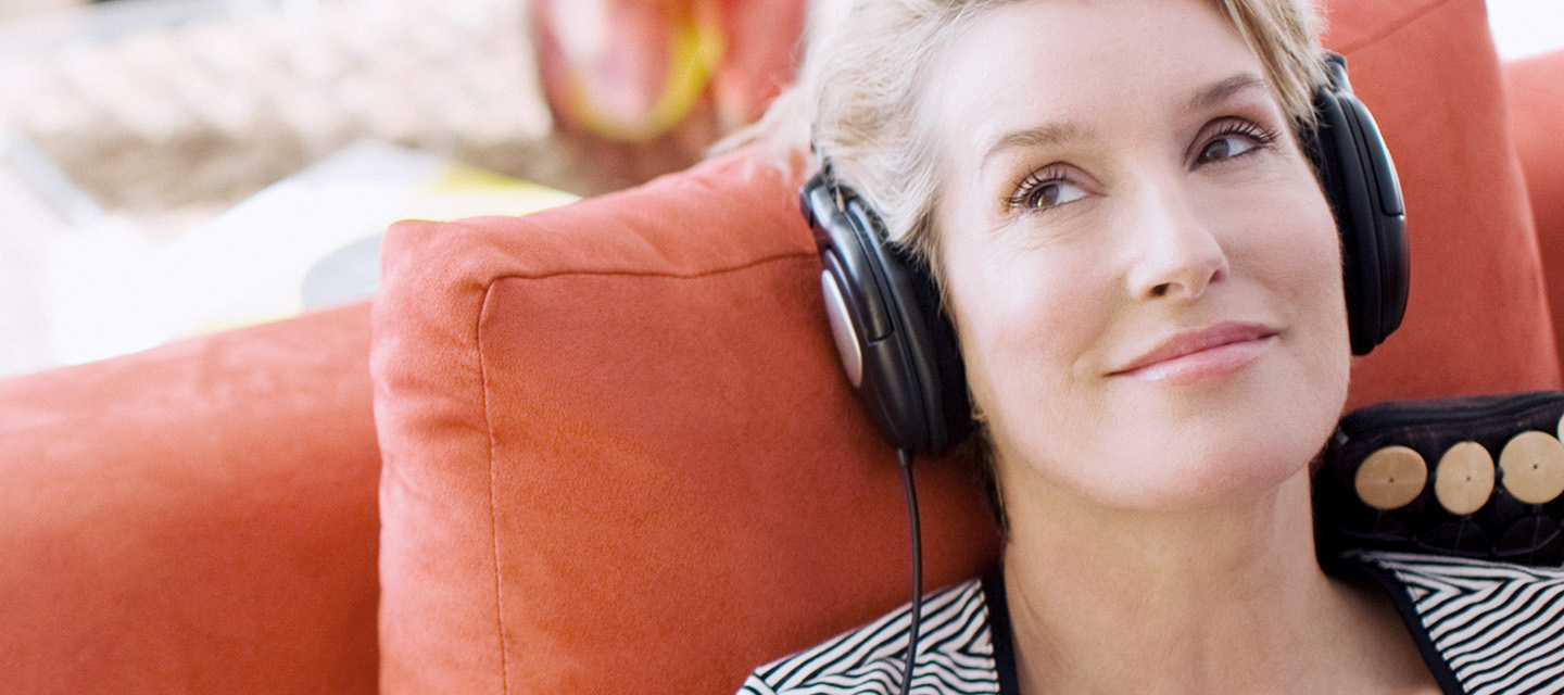 Immunonkologie: Frau mit Kopfhörern im Sessel beim Podcast-Hören.