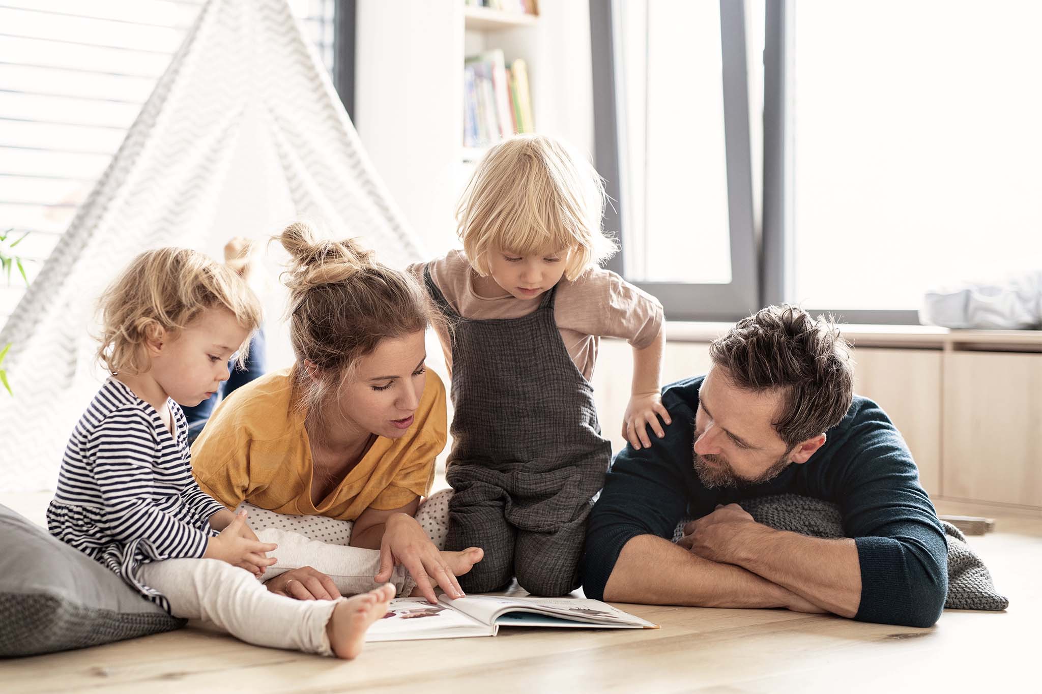 unge Familie mit zwei kleinen Kindern drinnen im Schlafzimmer lesen ein Buch.