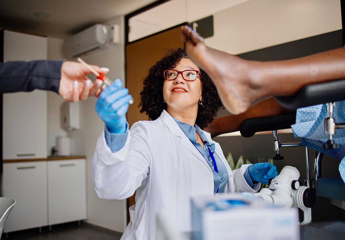 Ärztin mit blauen Handschuhen bereitet einen Abstrich während einer gynäkologischen Untersuchung einer Patientin in Beinstützen vor.