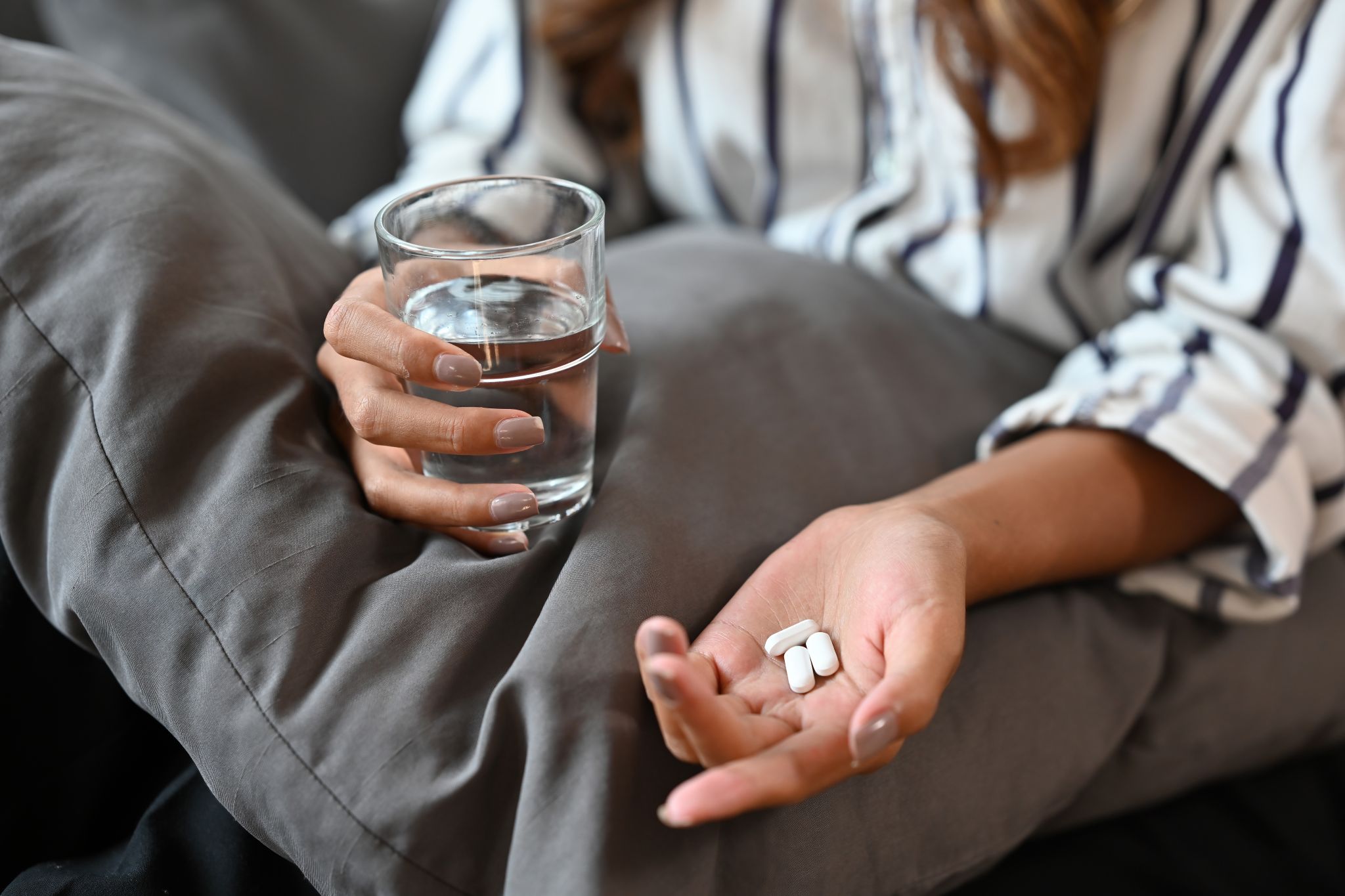 Nahansicht der Hände einer Frau, die Tabletten und ein Glas hält.