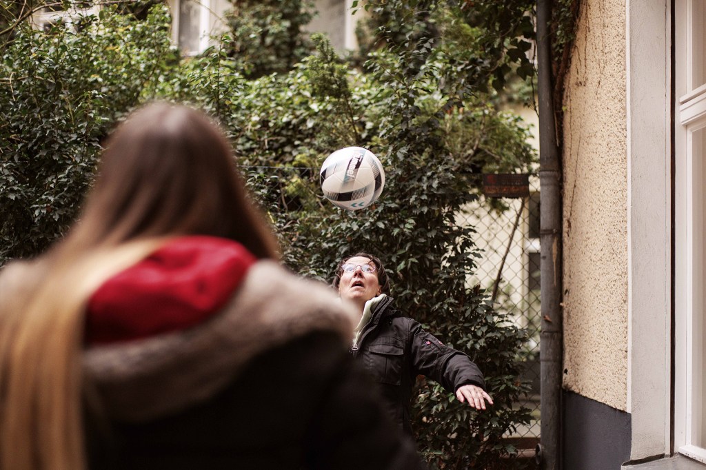 Patrycja und ihre Tochter spielen draußen Fußball. Patrycja schaut in die Luft auf den Fußball.