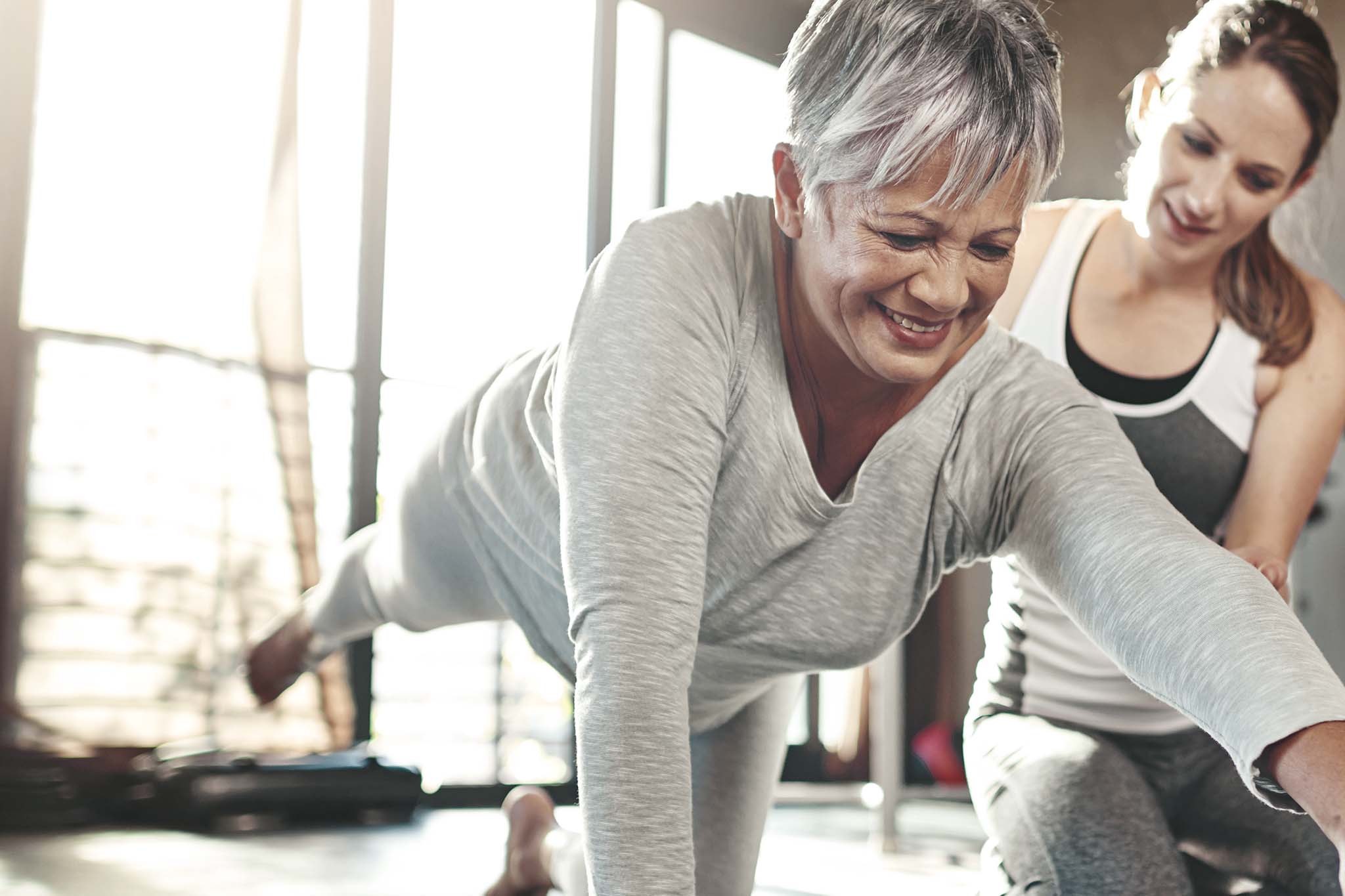 Eine ältere Patientin wird während der Reha nach Krebs von einer Physiotherapeutin bei Gymnastikübungen begleitet.