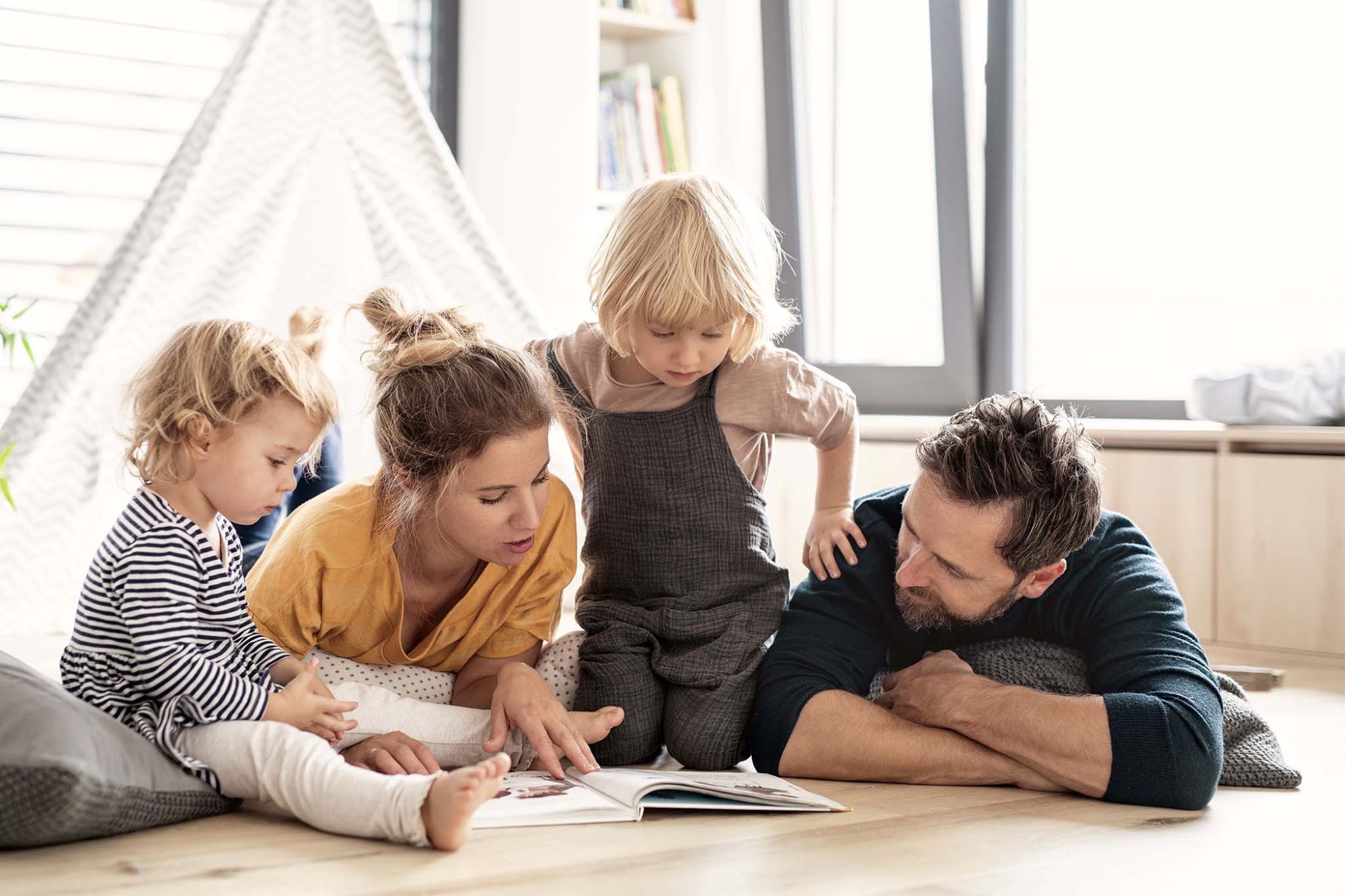 Junge Familie mit zwei kleinen Kindern drinnen im Schlafzimmer lesen ein Buch.