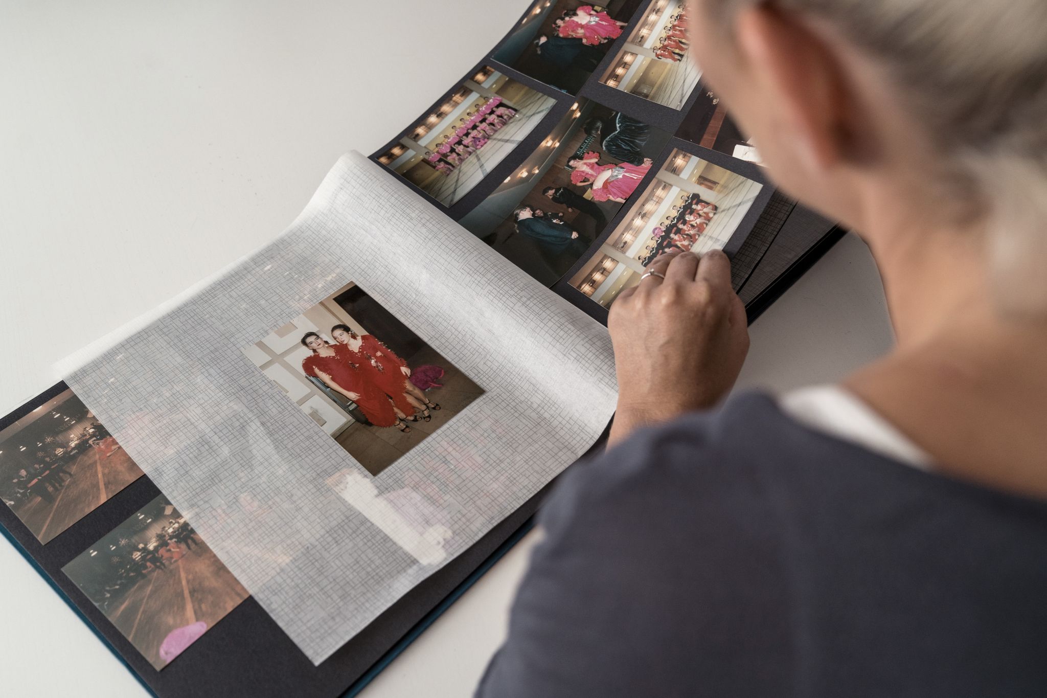 Moni sitzt an einem Tisch mit einem Fotoalbum vor sich und schaut Fotos von sich früher in der Tanzschule an.