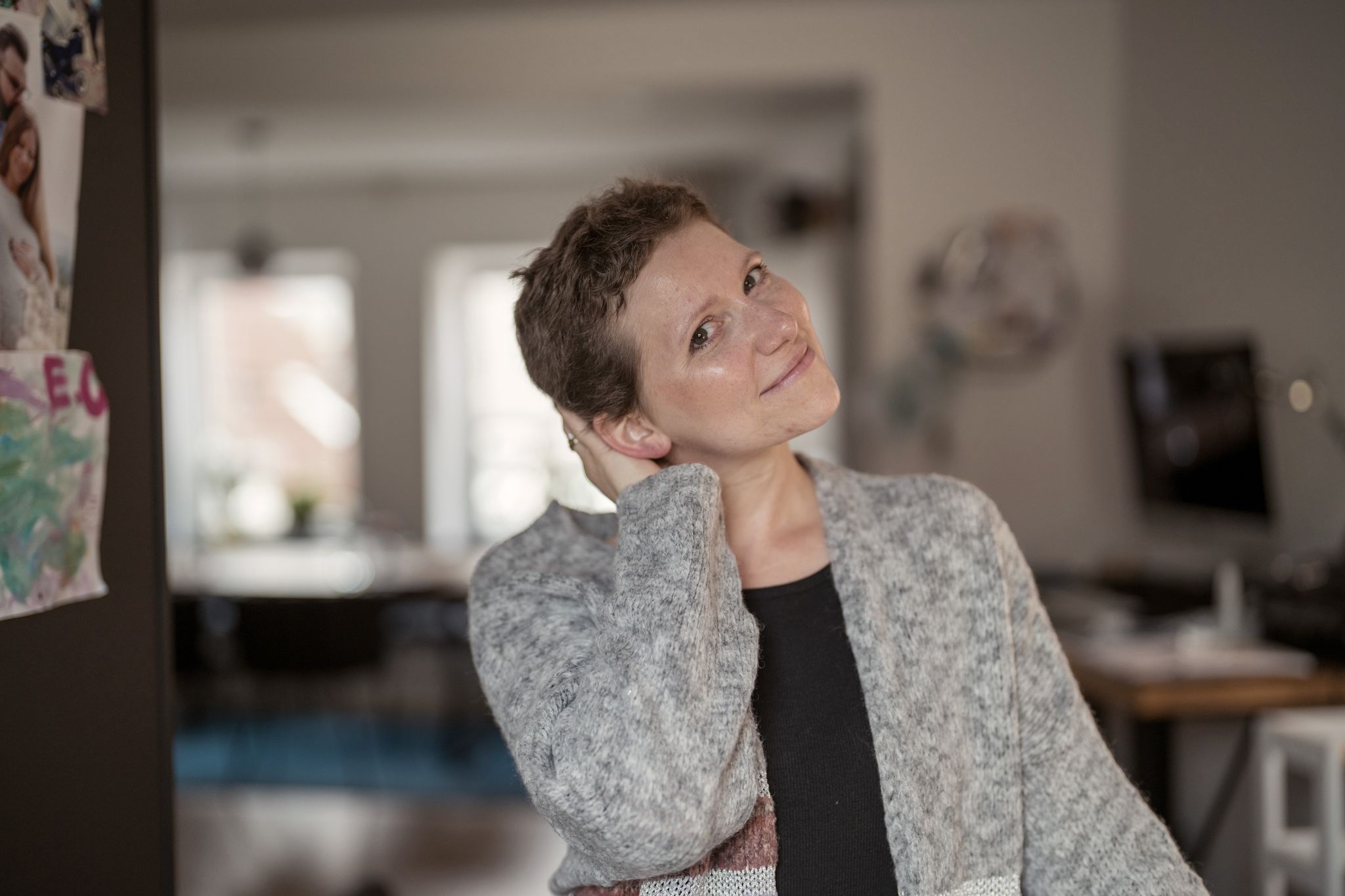 Silja steht neben ihrem Kühlschrank. Sie fasst sich in ihre kurzen, braunen Haare und lächelt mit schräg gehaltenem Kopf in die Kamera.