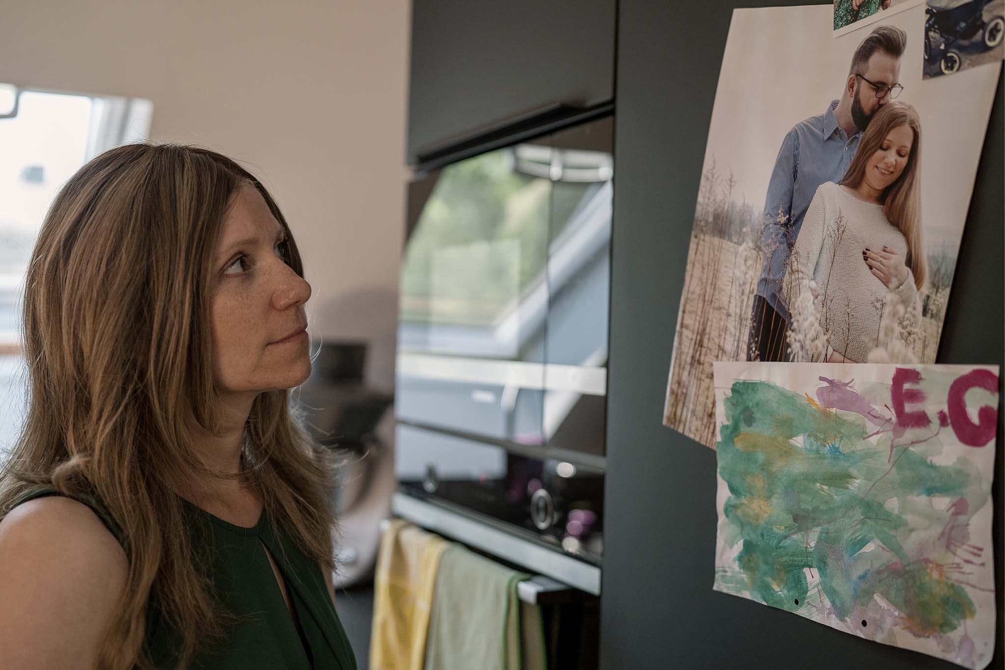Silja steht vor ihrem Kühlschrank. Sie betrachtet ein Foto, das mit einem Magneten befestigt ist. Es zeigt sie als Schwangere gemeinsam mit ihrem Mann.