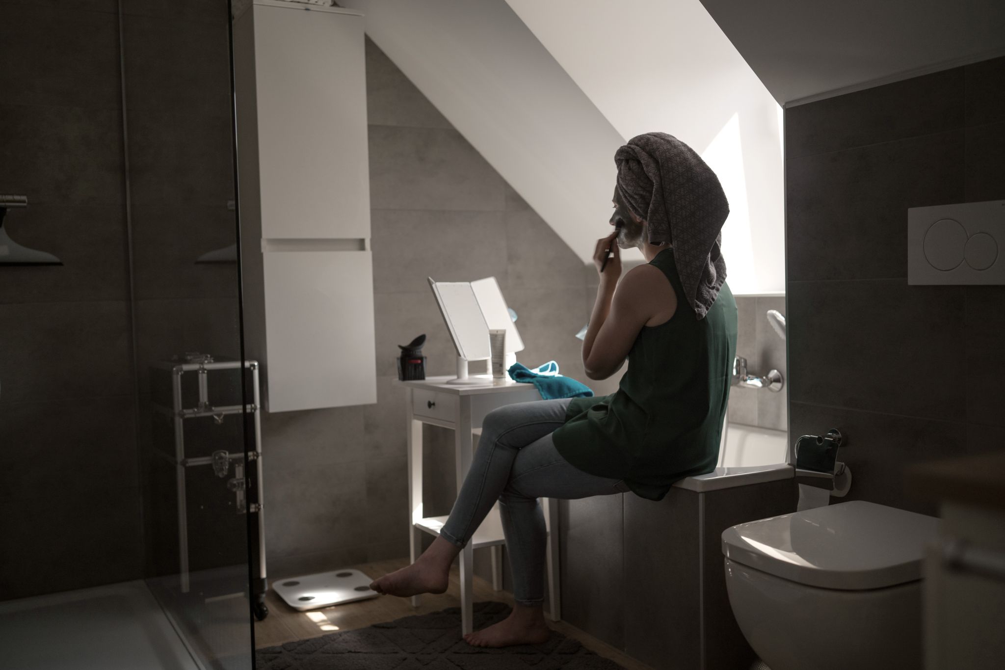 Silja sitzt auf dem Rand der Badewanne und trägt mit einem Pinsel ein Beautyprodukt auf ihr Gesicht auf.
