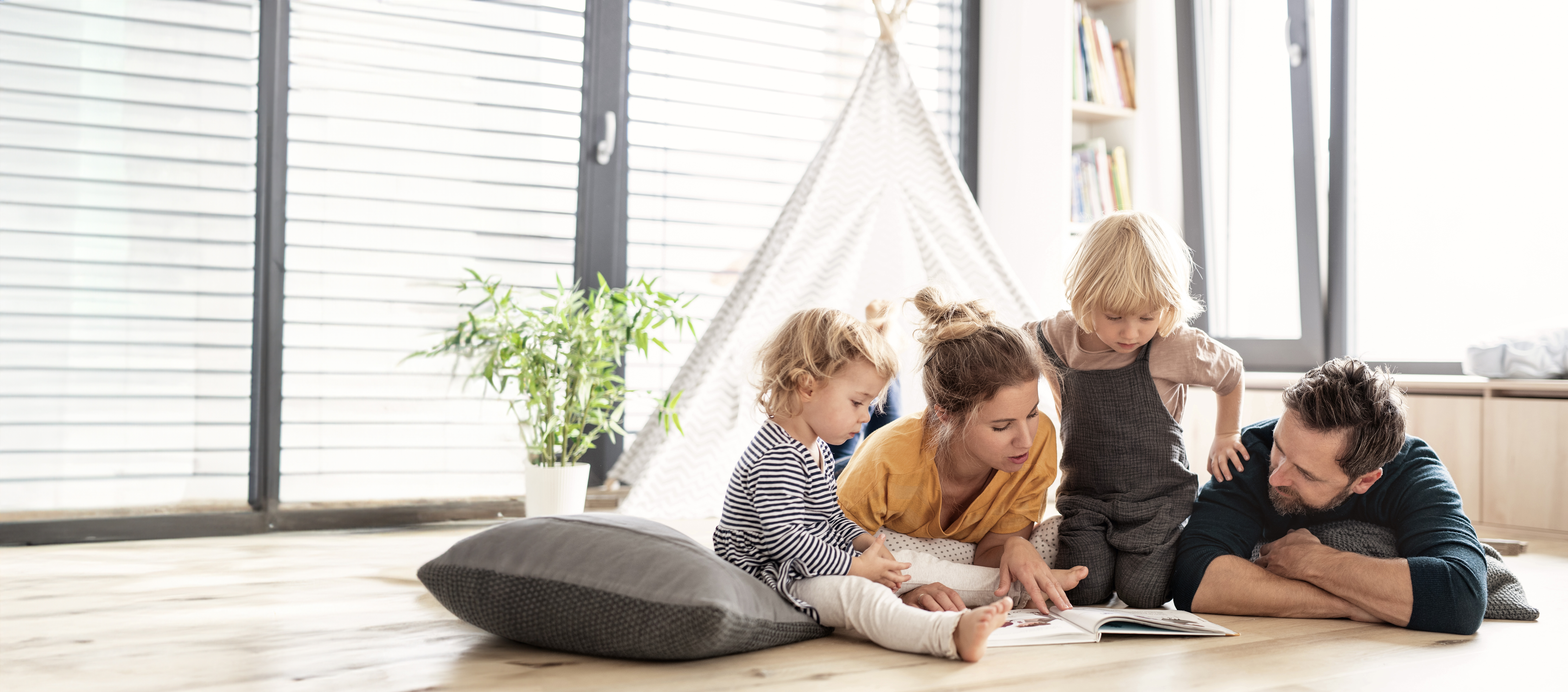 Junge Familie mit zwei kleinen Kindern drinnen im Schlafzimmer lesen ein Buch.