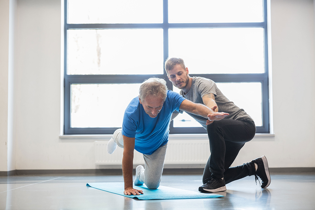 Ein Mann hilft einem Patienten bei Übungen auf einer Gymnastikmatte