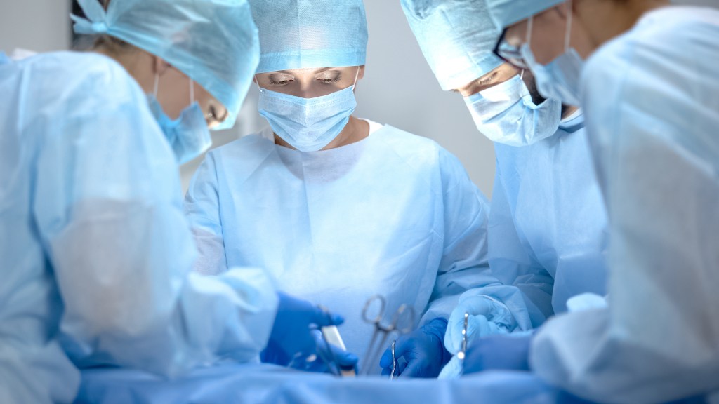 Das Foto zeigt ein Team von Chirurg:innen in blauen OP-Kitteln, Hauben und Gesichtsmasken, das eine Operation durchführt. Die zentrale Person blickt konzentriert auf das Operationsfeld, während die anderen assistieren.