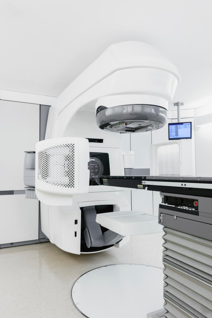 Das Foto zeigt ein modernes Bestrahlungsgerät in einem medizinischen Behandlungsraum, das für die Strahlentherapie in der Krebsbehandlung eingesetzt wird.
