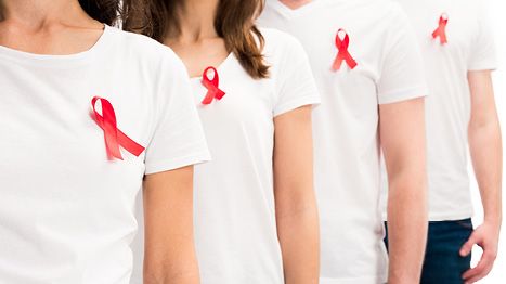 Hintereinander stehende Menschen, die eine AIDS-Schleife auf ihren T-Shirts tragen.