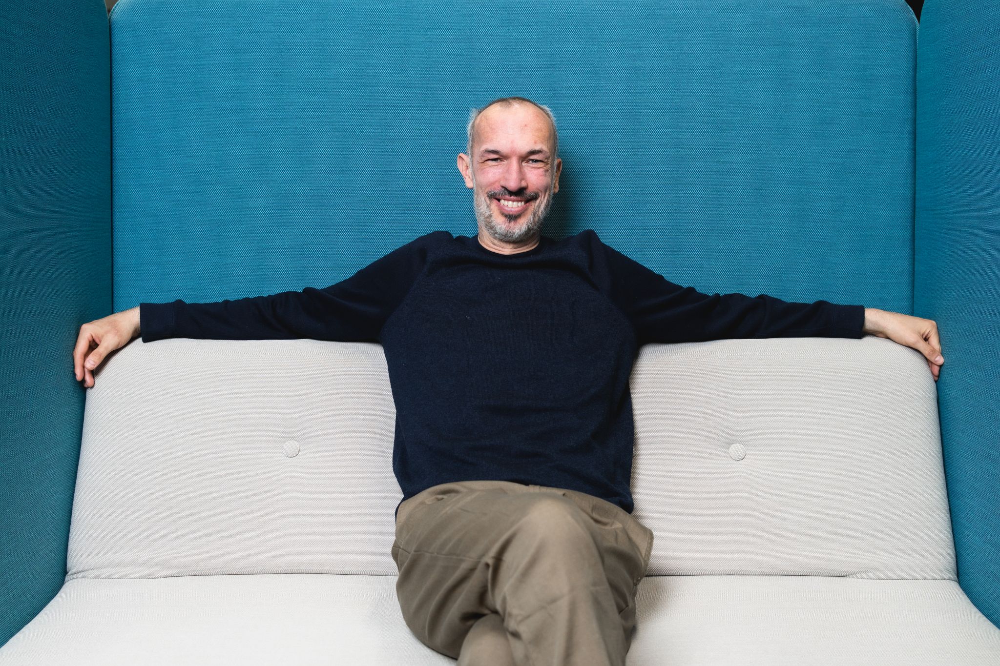 Andi sitzt auf einem Sofa und lächelt in die Kamera