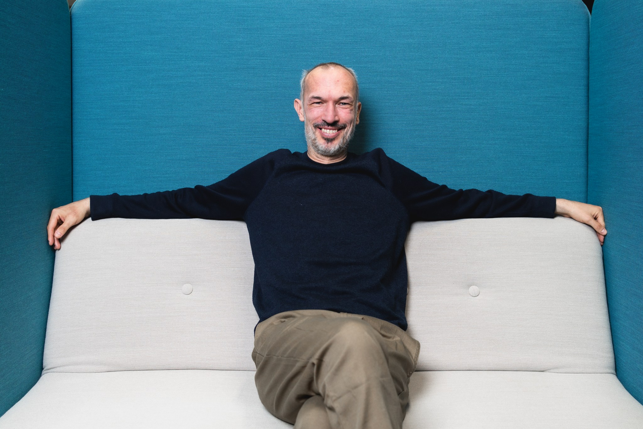 Andi sitzt auf einem Sofa und lächelt in die Kamera