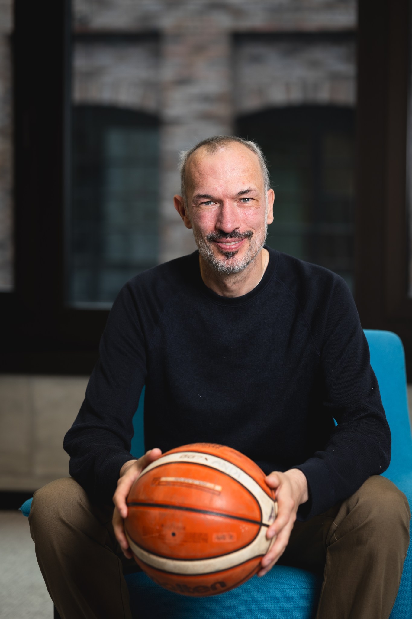 Zu sehen ist Andi, der mit einem Basketball in der Hand auf einem Sessel sitzt.