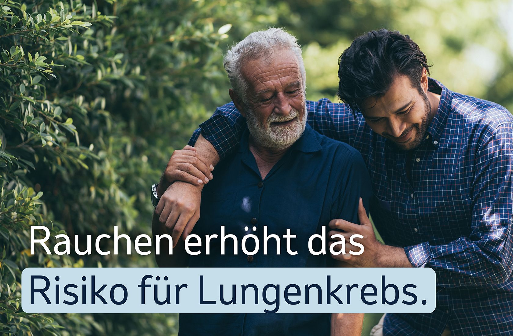 Junger Mann legt den Arm um einen älteren Mann im Grünen, mit dem Text „Rauchen erhöht das Risiko für Lungenkrebs.“